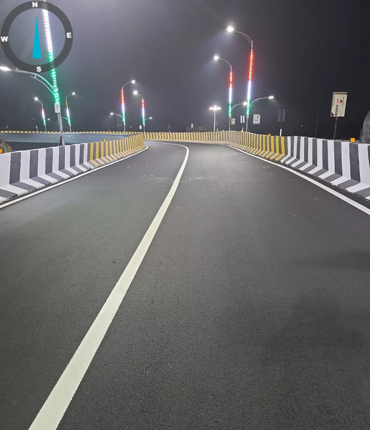 Completed road marking on a curving flyover carriageway at night, chevron parapets and coloured LED lighting