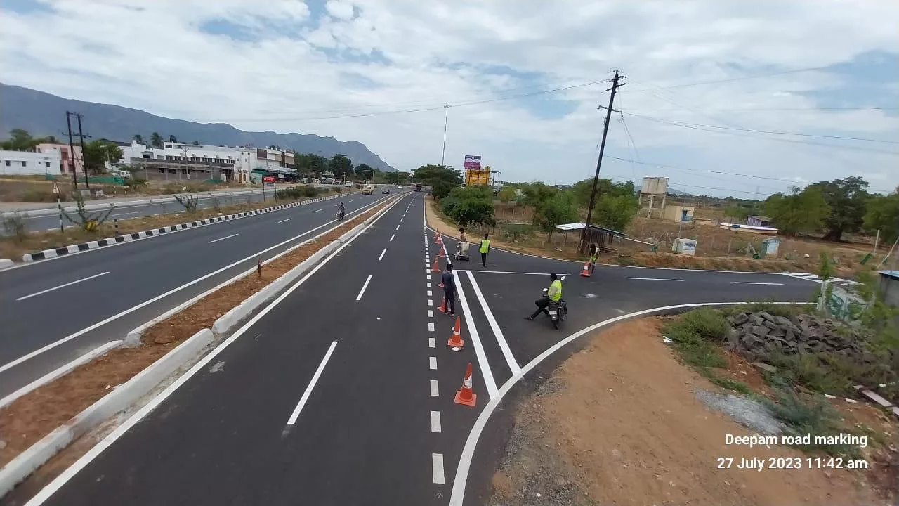 Road marking crew and traffic cones on a divided highway with a hill backdrop, Tamil Nadu