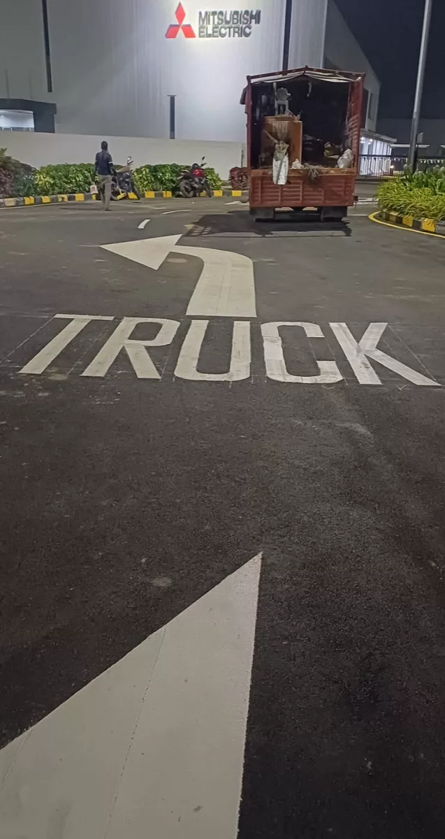TRUCK directional arrow road marking at an industrial facility (Mitsubishi Electric signage visible)